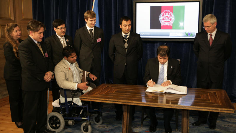 Afghanistan's Ambassador Jawed Ludin signs the Convention on Cluster Munitions in Oslo as cluster munition survivor Soraj Habib and other members of the Cluster Munition Coalition look on, December 3 (c) CCM, 2008